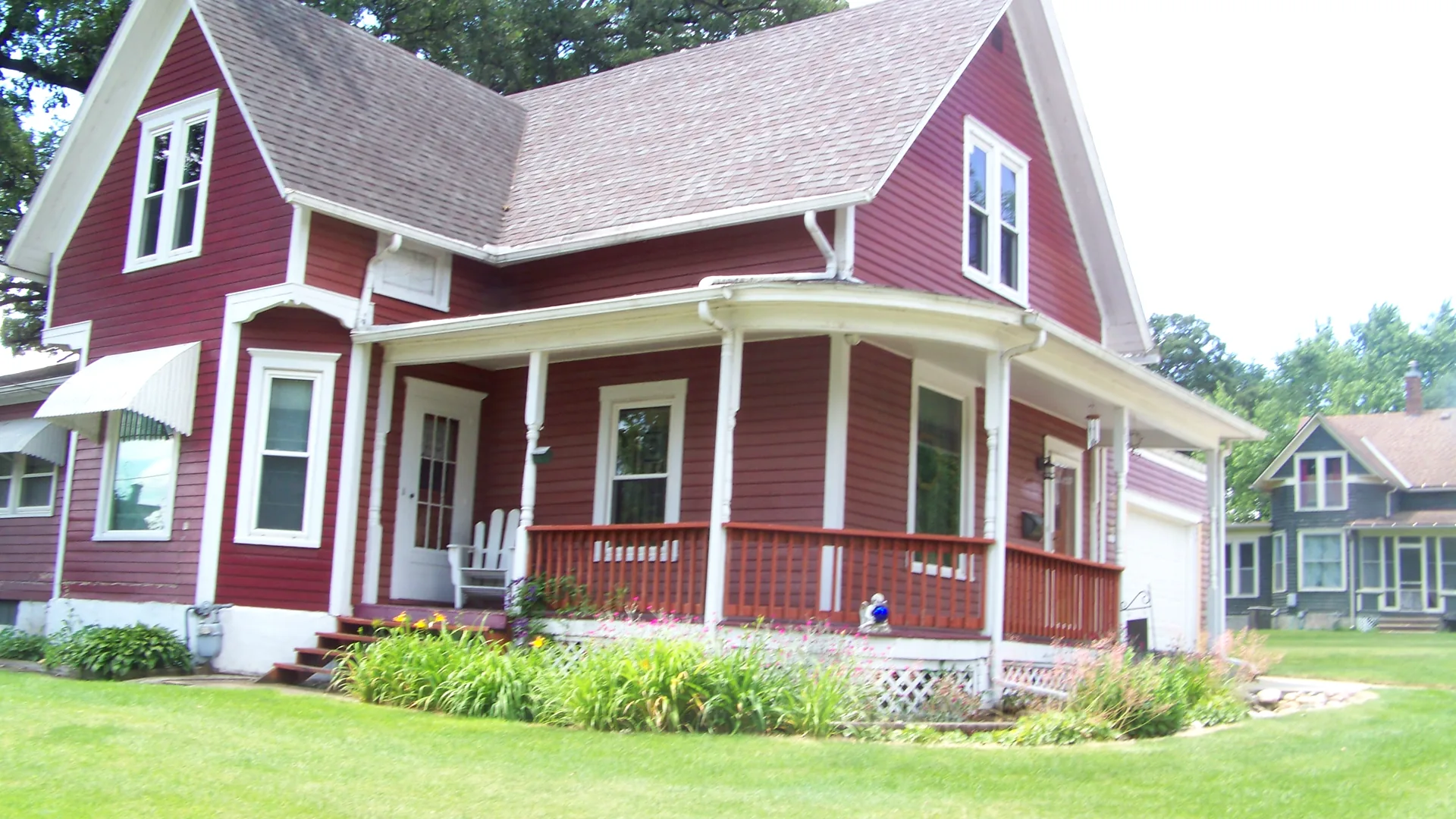 A red farmhouse with white trim and a wraparound porch, from the Hoskins Exteriors project gallery