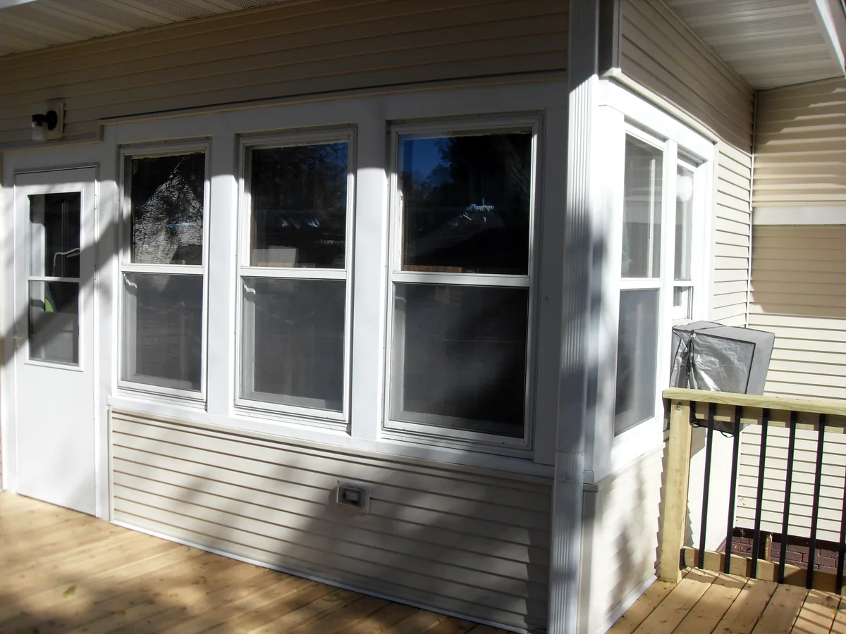 Enclosed porch with tall white windows above a new deck